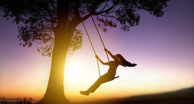 silhouette of happy young woman on a swing with sunset background