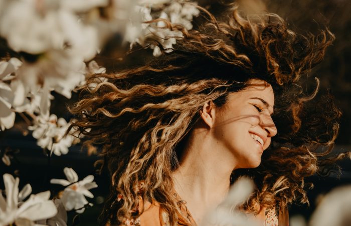 Alana Sousa/Pexels https://www.pexels.com/photo/happy-woman-with-curly-hair-near-flowers-7523506/