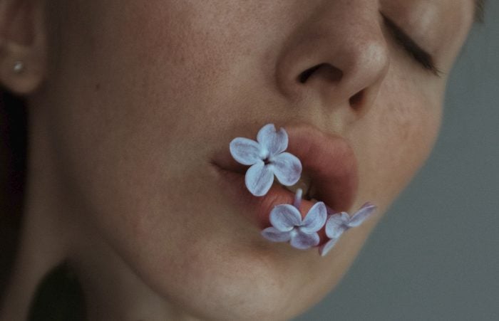 Anna Avilova/Pexels https://www.pexels.com/photo/close-up-shot-of-a-woman-with-lilac-flowers-on-her-mouth-4843400/